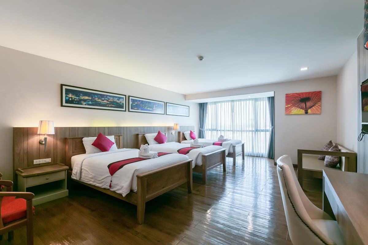 A hotel room with four single beds, wooden headboards, a wooden desk, and a large window with curtains.