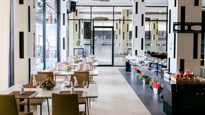 A modern dining area with long tables, chairs, and a central bar area with a marble countertop. - Grand Ratchapruek Hotel (Pak Kret)