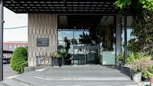A modern building entrance with a reception desk, a staircase leading to the lobby, and potted plants. - Grand Ratchapruek Hotel (Pak Kret)