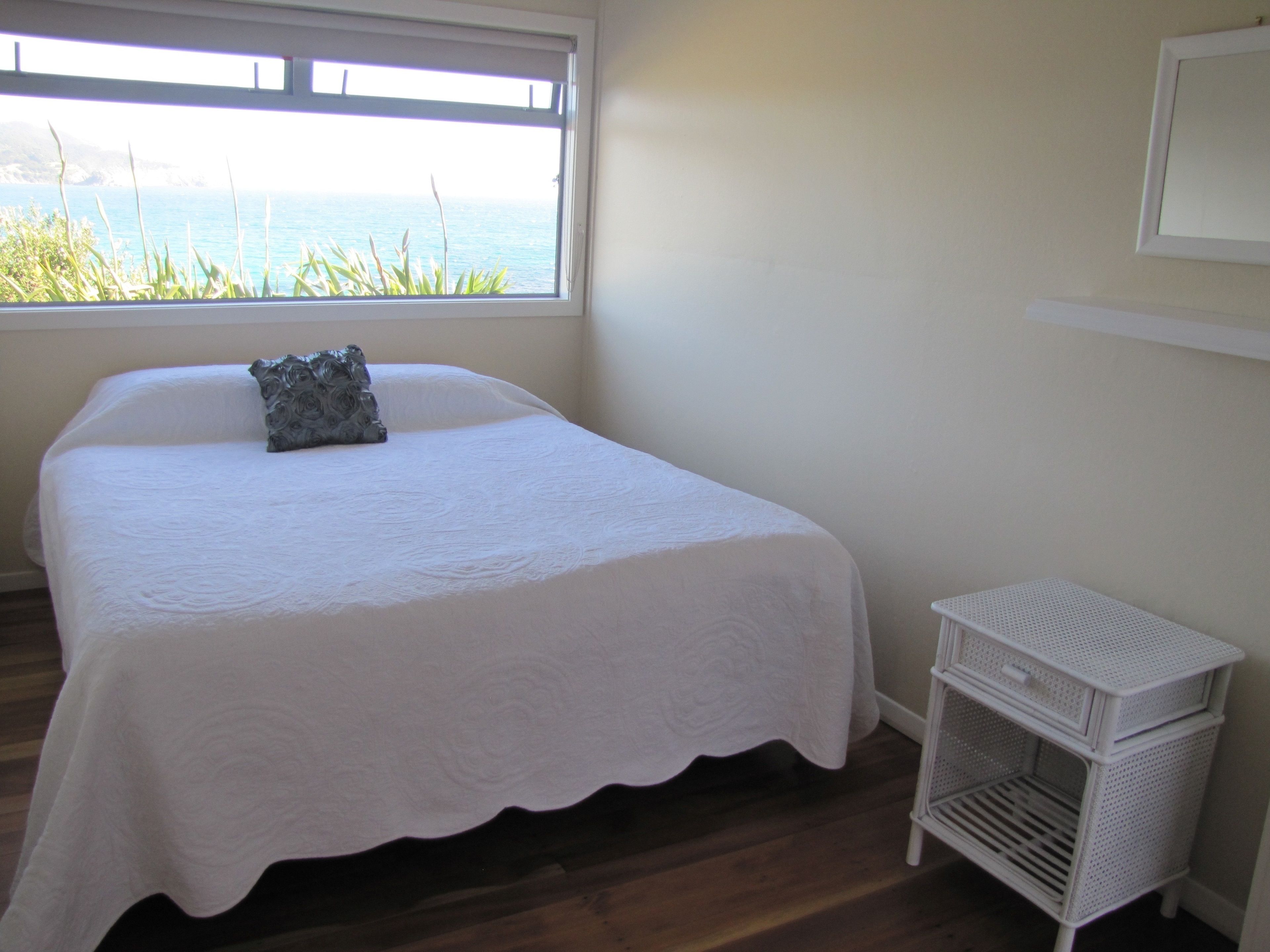 Un dormitorio con cama, ventana con vista al mar y un mueble blanco para guardar objetos.