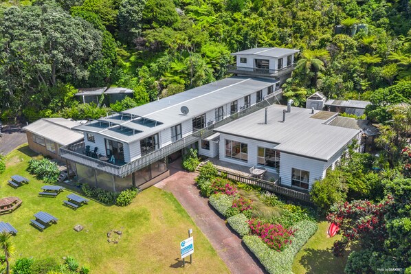 A modern building with a flat roof, large windows, and a covered outdoor area with seating. - Tipi and Bob's Waterfront Lodge (Great Barrier Island)