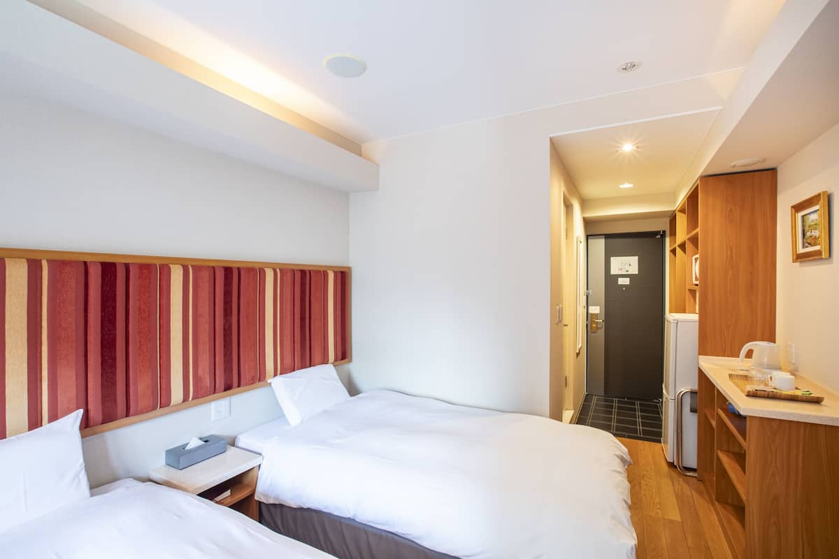 A hotel room with two beds, a wooden headboard, a small desk, and a kitchenette area.