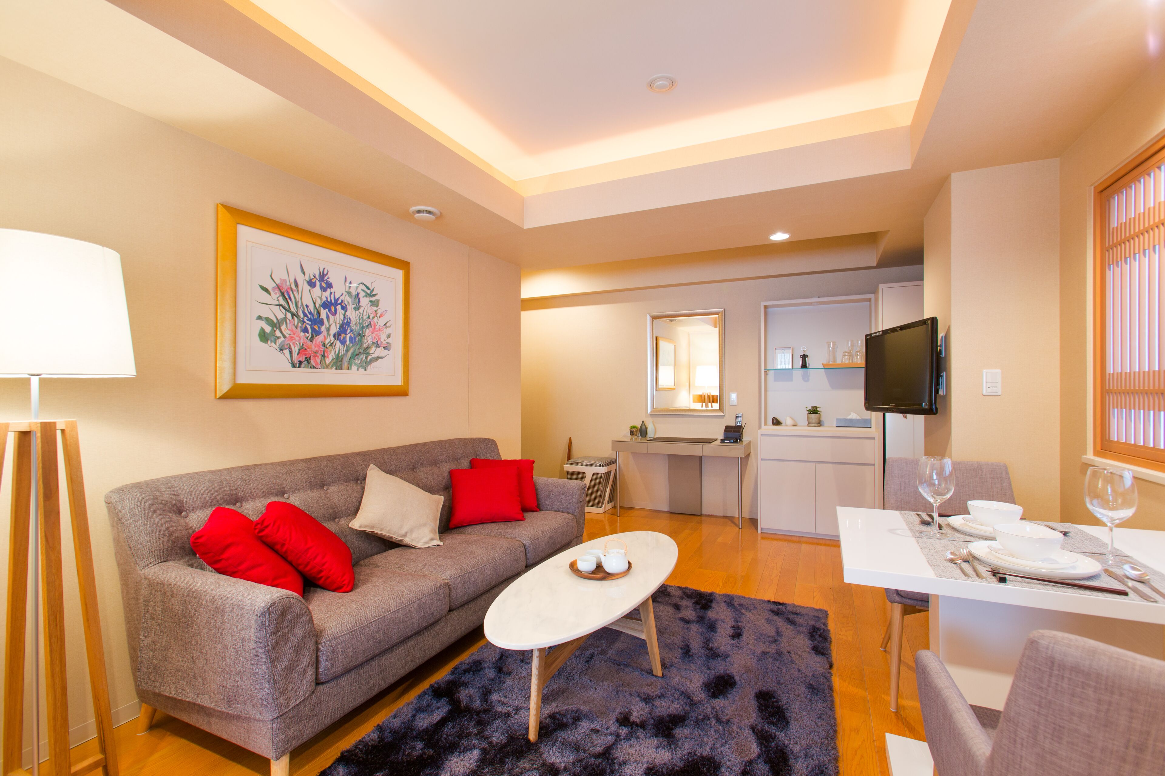 A modern living room with a grey sofa, red cushions, a coffee table, and a dining area with a white table set for two.