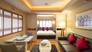 A hotel room with a bed, a sofa, a dining table with chairs, a coffee table, and a window with blinds. - M Hotel (Kutchan)