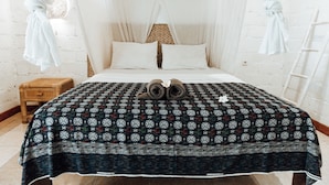 A bed with a patterned bedspread, a pair of rolled-up towels, and a wooden nightstand.
