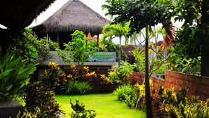 A tropical garden with a thatched-roof structure, lush greenery, and a sign for 'Warung Froggy'.