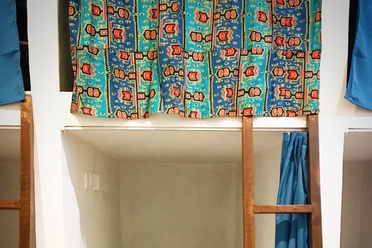 A bunk bed with a patterned curtain and a single rolled towel.