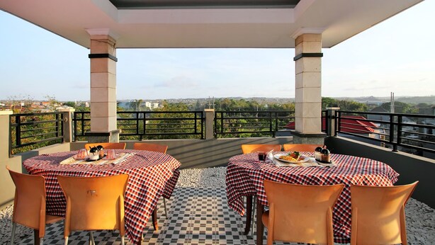 Un área de comedor al aire libre con manteles a cuadros y sillas anaranjadas, con vista a un paisaje urbano.