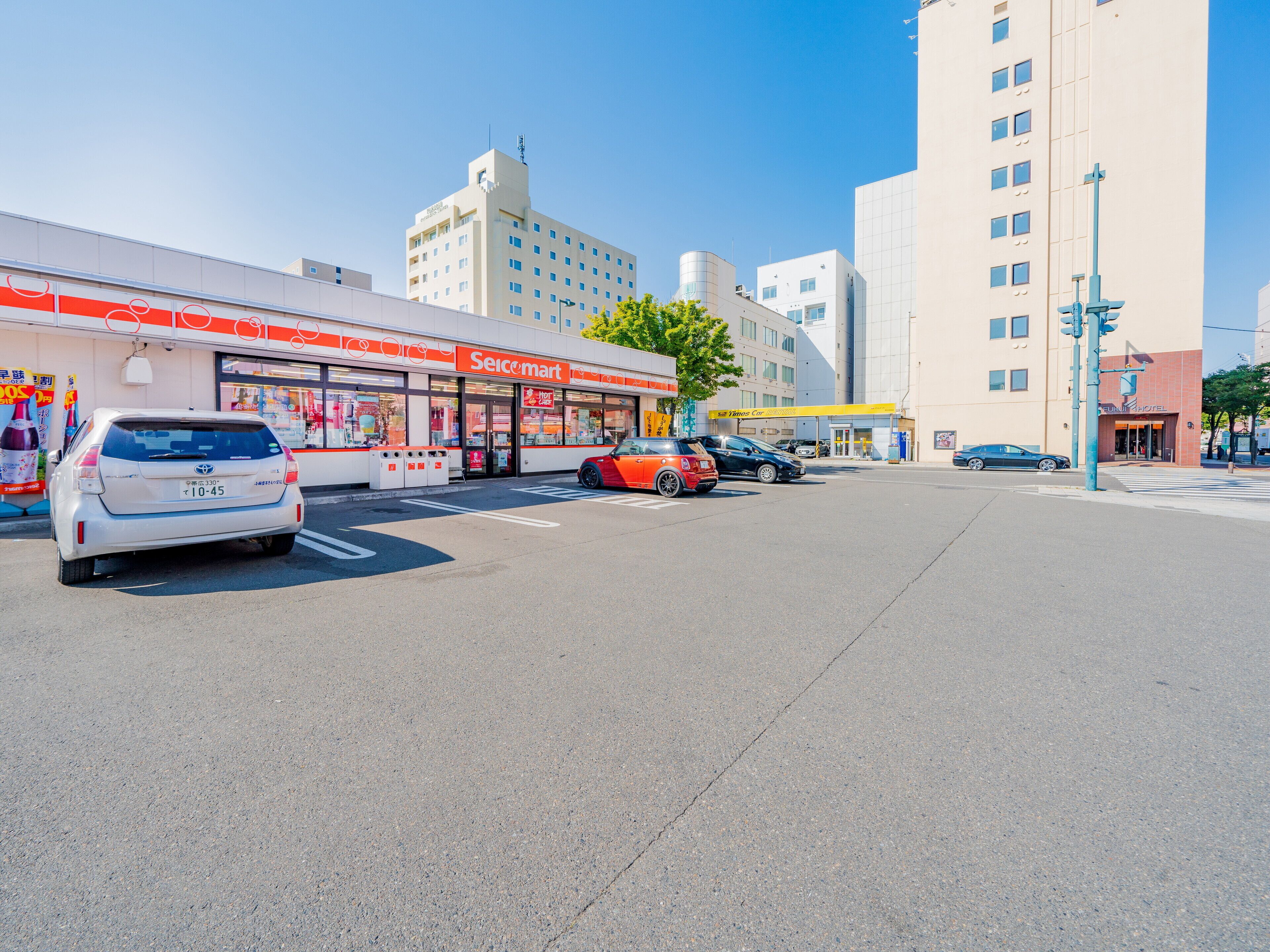 Una tienda Seimart con un estacionamiento, un coche rojo y un coche blanco.