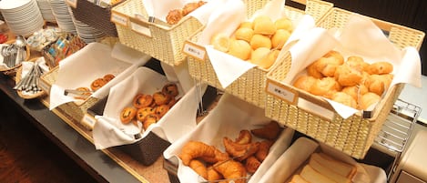 A buffet with various food items including bread, pastries, and rolls.