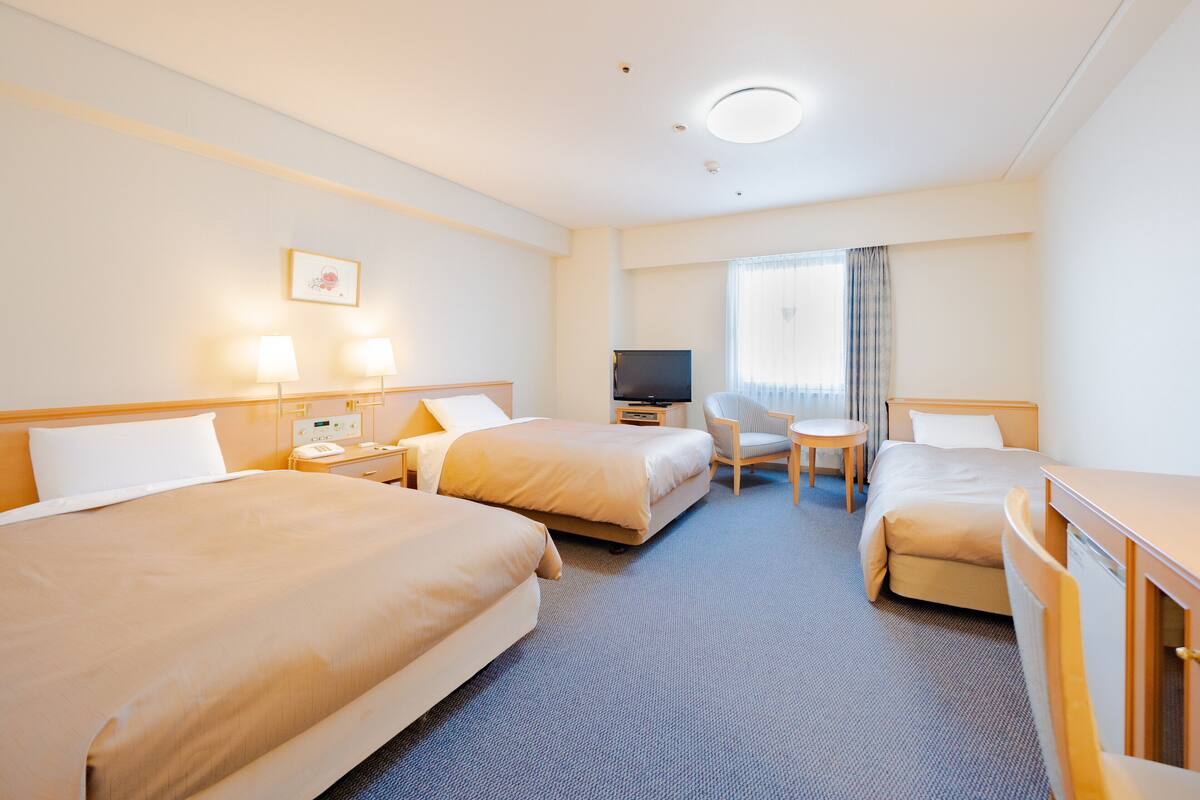 A hotel room with two beds, a TV, a small table, and a chair.