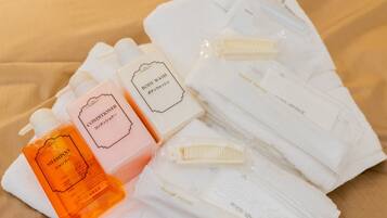 Un set ordinato di articoli da toilette, tra cui shampoo, balsamo, bagnoschiuma e spazzolino, tutti confezionati in contenitori bianchi e arancioni.
