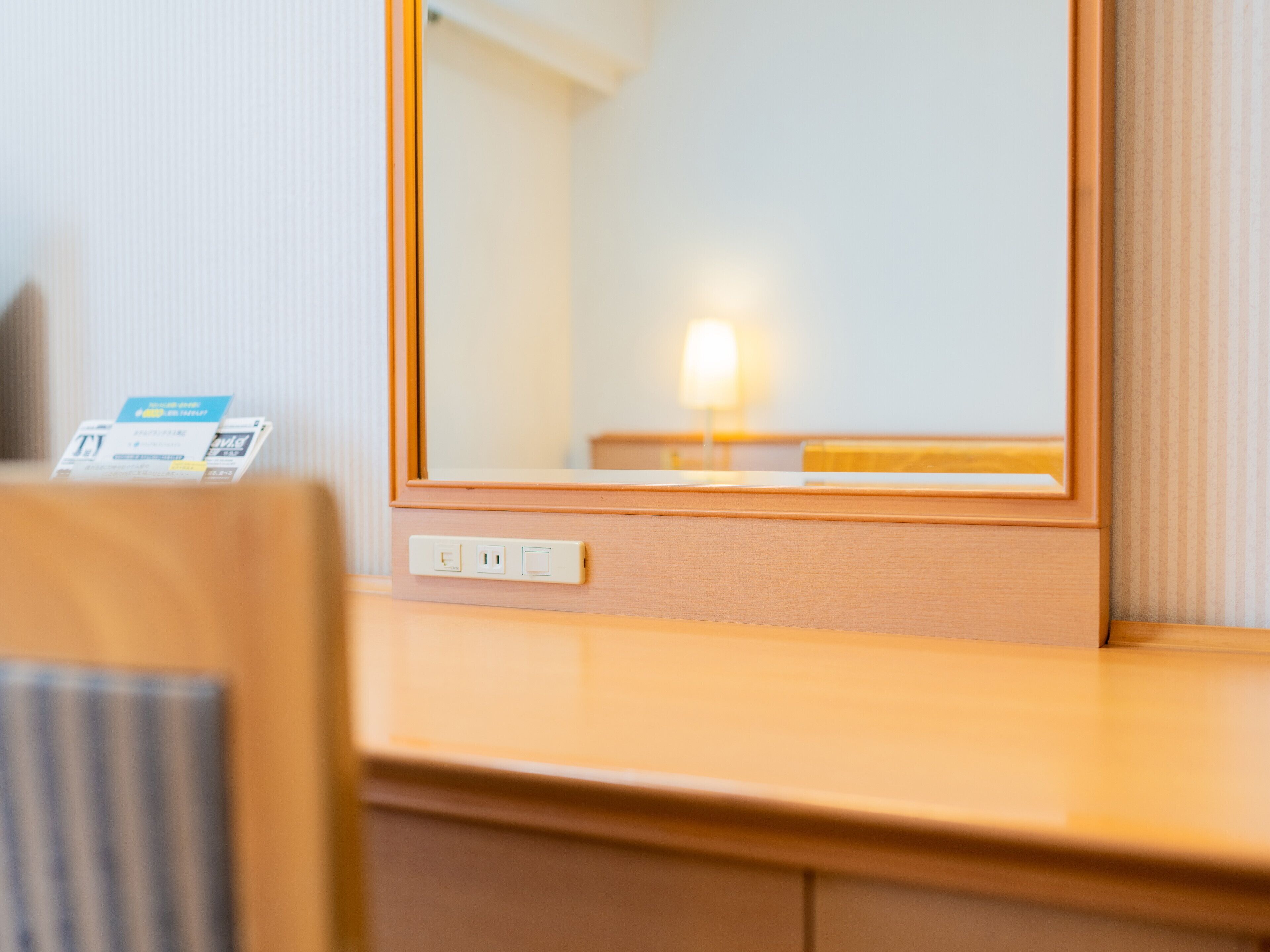 Una habitación de hotel con un escritorio de madera, un espejo y una lámpara.