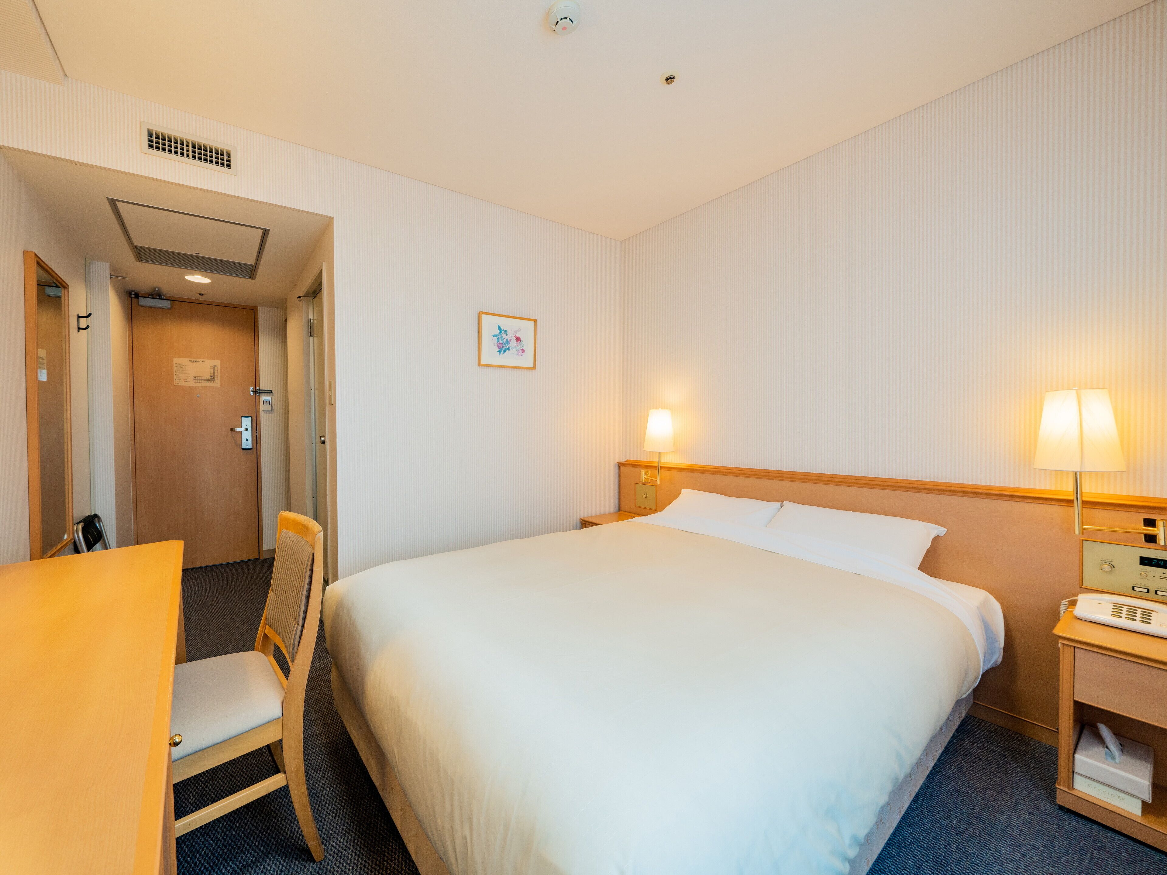 Una habitación de hotel con una cama, una silla, un escritorio y una mesita de noche con lámpara.