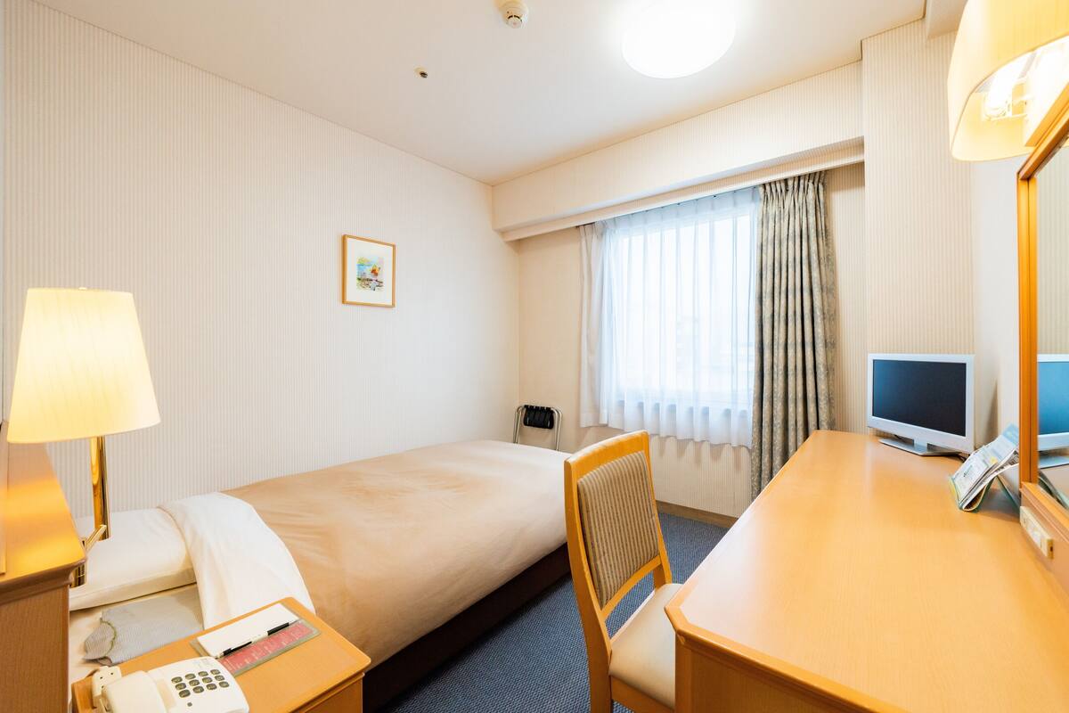 A hotel room with a bed, a desk with a computer, a telephone, and a chair.