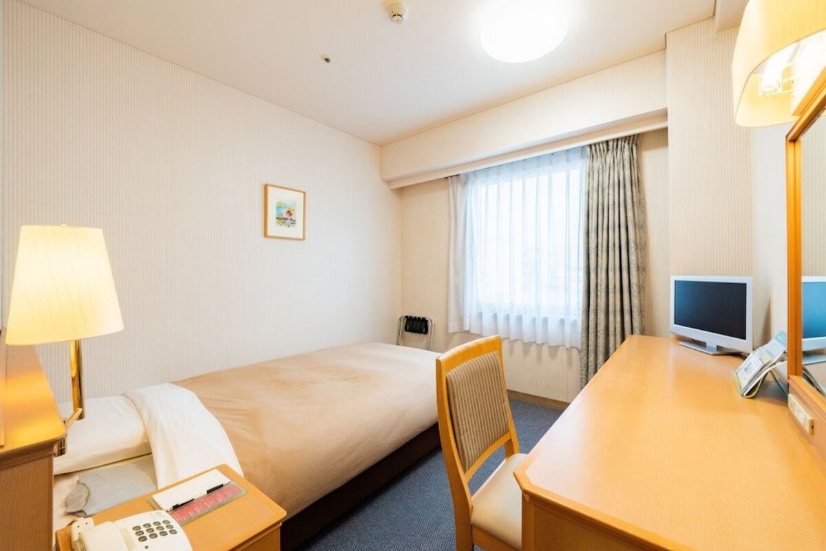 Habitación de hotel con dos camas, un escritorio, una silla, un teléfono, un televisor y una ventana con cortinas.