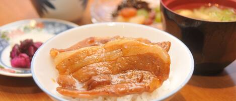 A bowl of rice topped with a glazed meat dish, accompanied by a small plate of pickled vegetables and a bowl of soup.