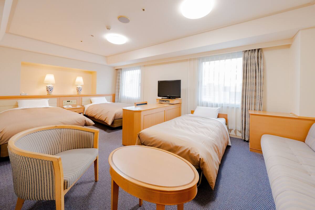 A hotel room with two beds, a desk, a television, and a seating area with a chair and a small table.