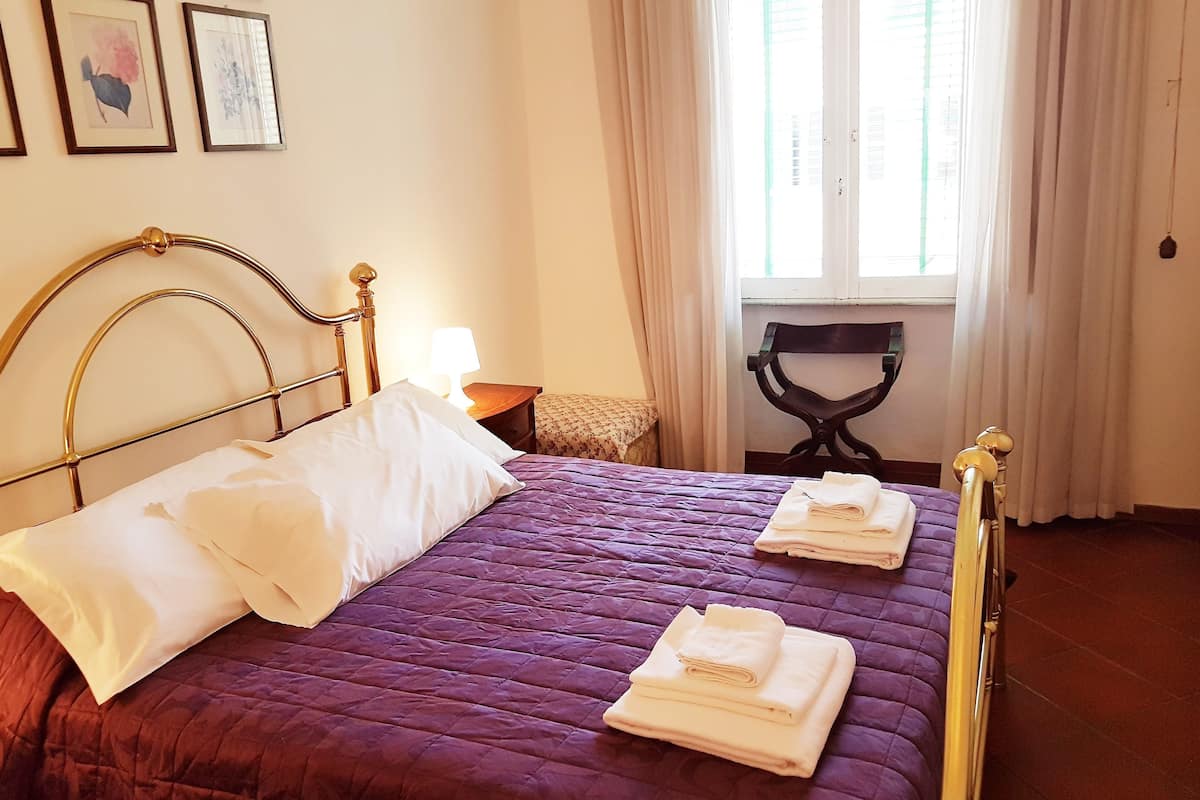 A neatly made bed with a purple bedspread, white pillows, and folded towels.