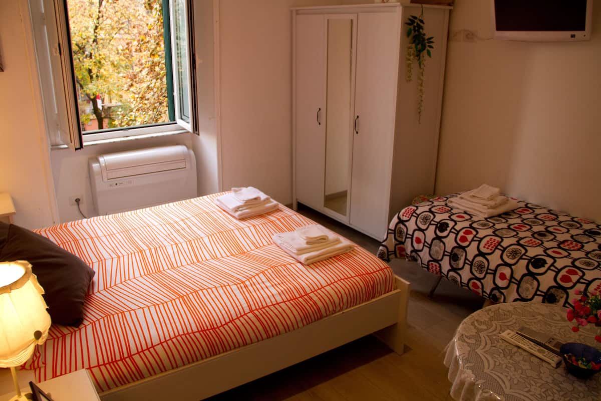 A bedroom with a bed, a bedside table, a lamp, a wardrobe, and a window.