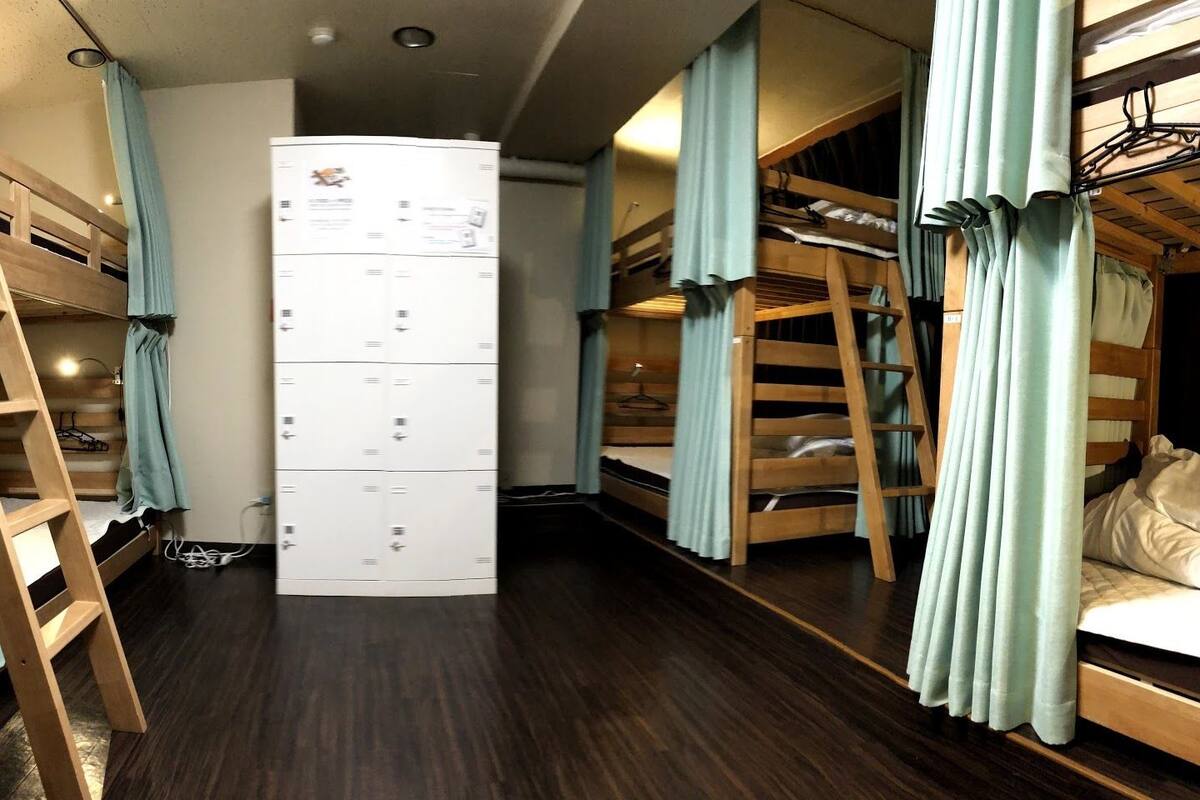 Quarto compacto com beliches, um armário central e cortinas.