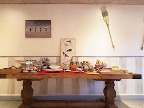 A long wooden table with various food items and a bird illustration on the wall. - L'île aux Oiseaux (Andernos-les-Bains)