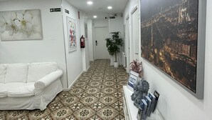 Un pasillo con baldosas de diseño, un sofá blanco, un cuadro grande de un paisaje urbano enmarcado y una consola blanca con revistas.