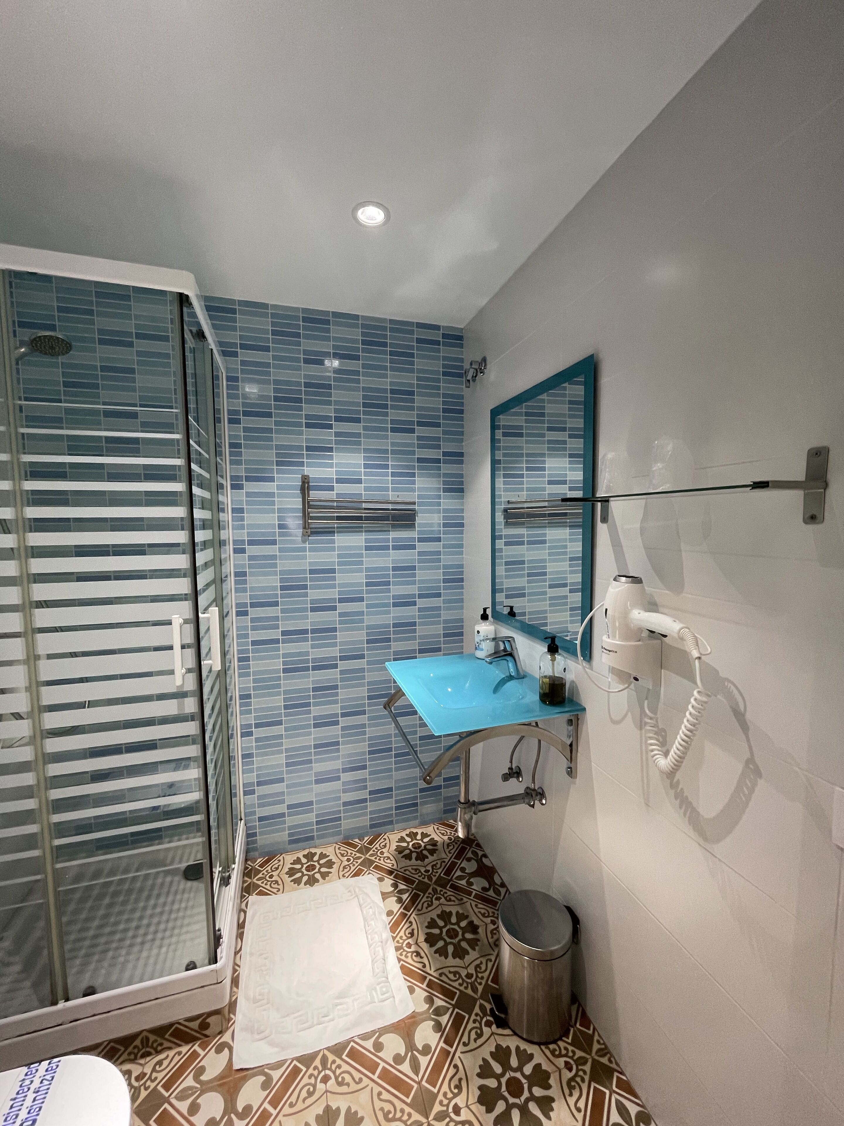 Un baño con cabina de ducha de vidrio, un lavamanos azul y un secador de pelo montado en la pared.