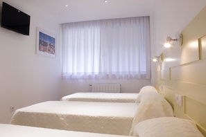 A hotel room with two beds, a mounted TV, a window with sheer curtains, and wall-mounted lighting. - Hostal Nova (Barcelona)