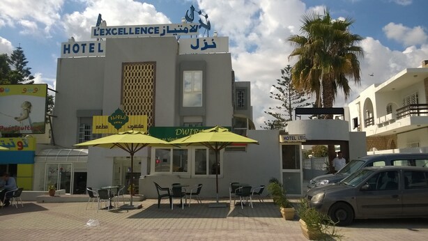 A hotel with outdoor seating and a sign in multiple languages. - Hôtel L´Excellence (Ariana)