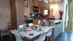 A cozy kitchen with a dining table set for four, surrounded by white chairs. There is a green island with various kitchen items and a clock on the wall. - B&B Emma (Bruges)