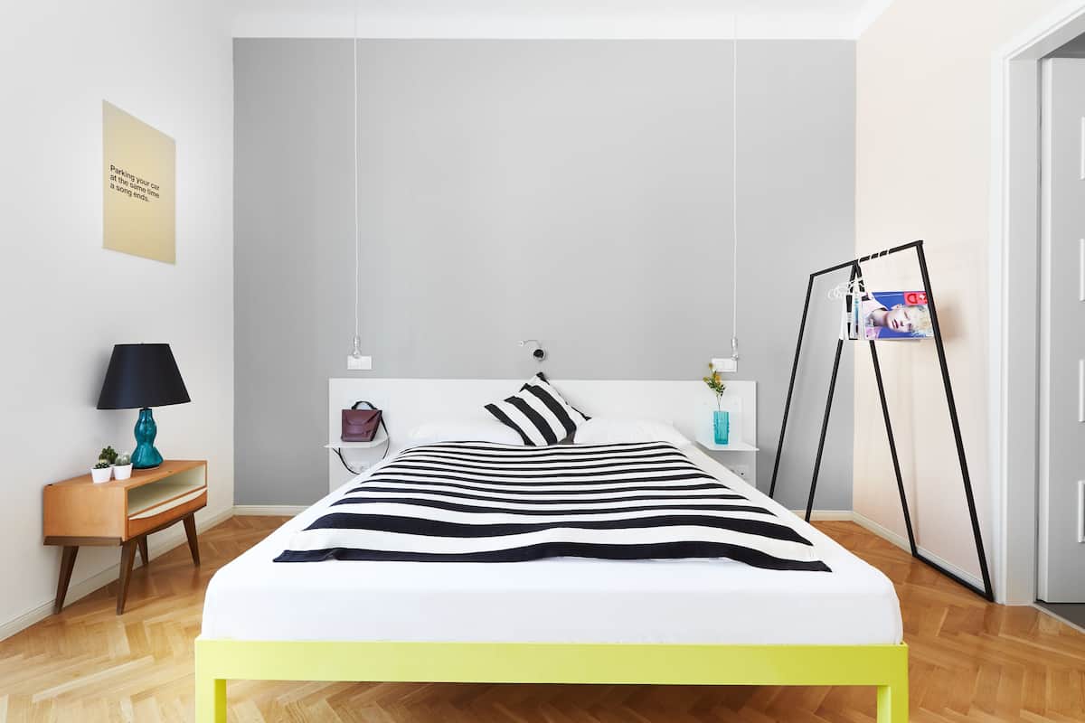Moderni makuuhuone, jossa on sänky, yöpöytä, lamppu ja seinälle kiinnitetty valokuvakehys.