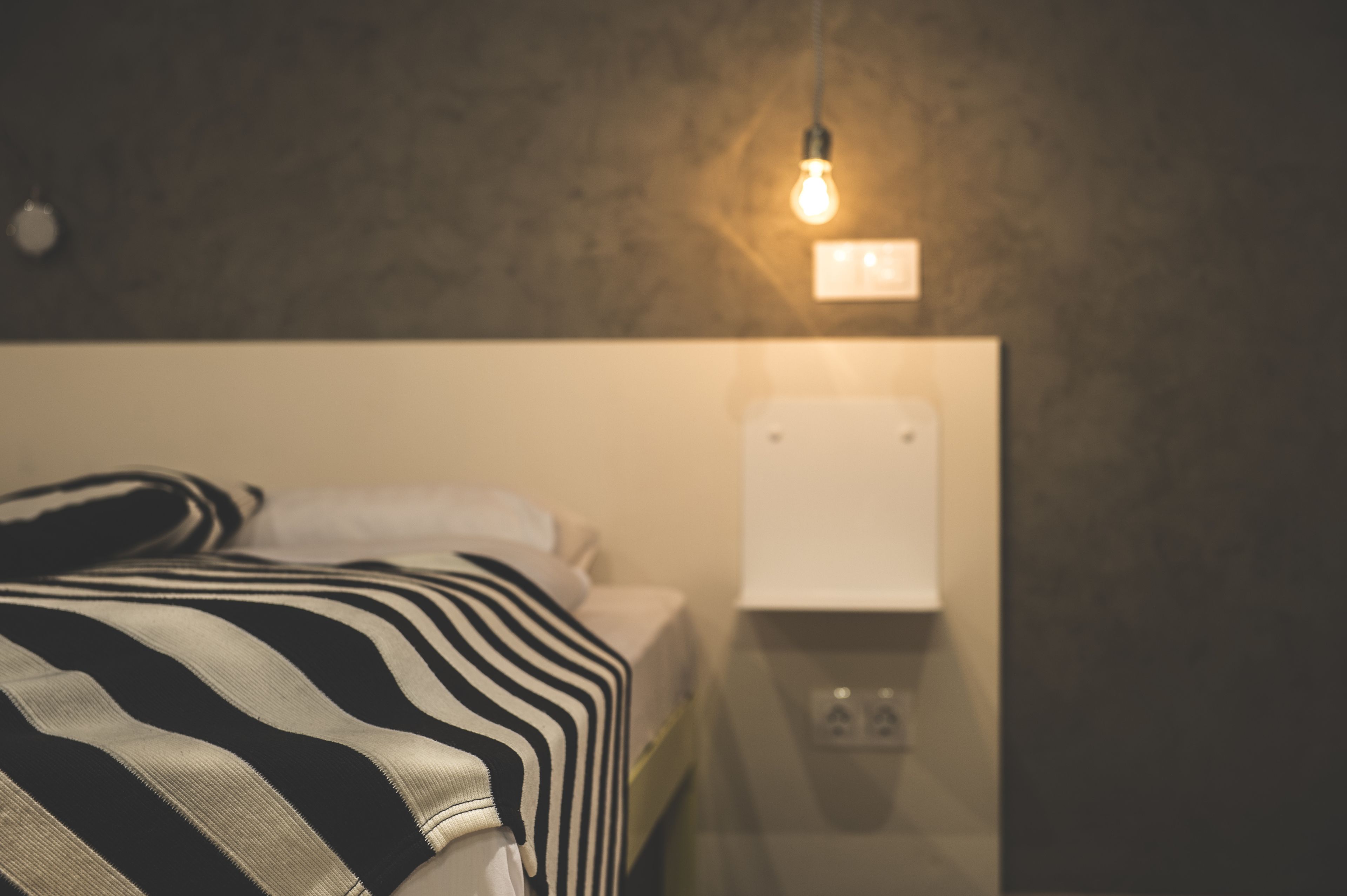 A bed with a striped blanket, a wall socket, and a light bulb.