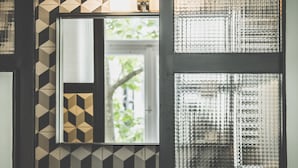 A door with geometric patterned tiles, a mirror reflecting a window, and frosted glass panels. - MGZN Basilica Rooms (Budapest)