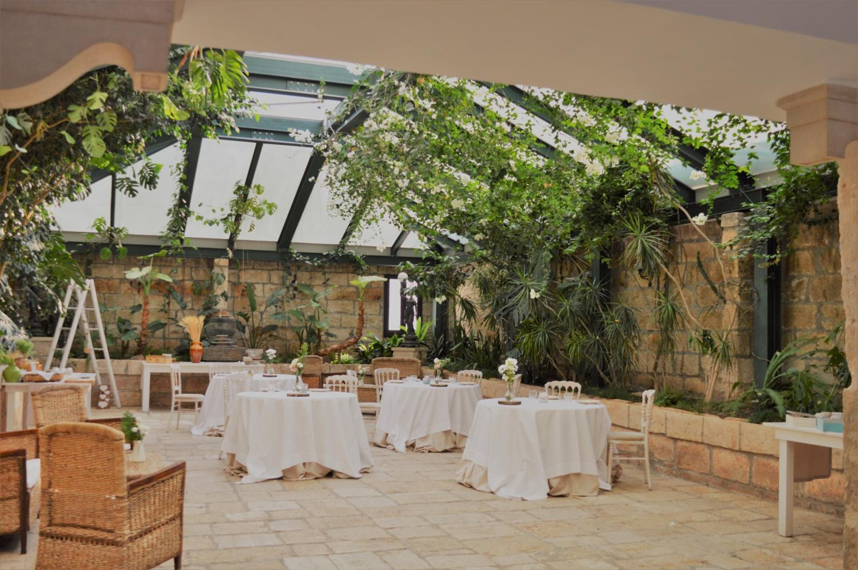 Une terrasse extérieure avec des tables disposées pour les repas, entourée d’une végétation luxuriante et de murs en pierre.
