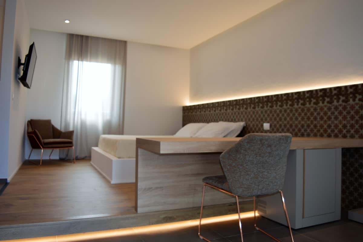 A modern bedroom with a bed, a desk, a chair, and a TV mounted on the wall.