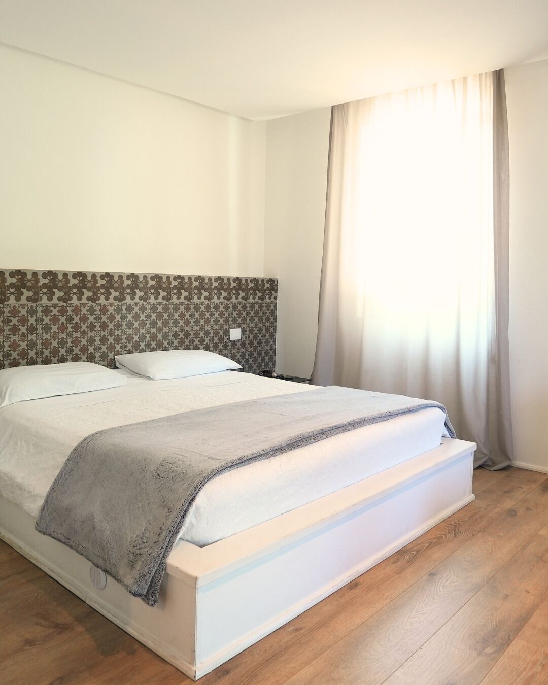 Ein ordentlich bezogenes Bett mit grauer Decke, einem gemusterten Kopfteil und Holzboden.