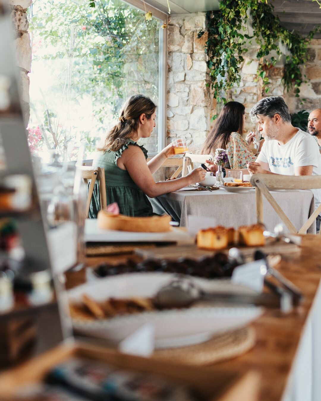 Un espace de restauration extérieur rustique, avec des murs en pierre et de la verdure, comprenant une table en bois sur laquelle sont disposés des plats et des boissons.