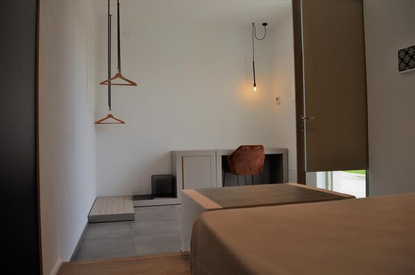 Un dormitorio moderno con cama, mesita de noche y una silla. Hay un escritorio pequeño con silla y una lámpara colgante.