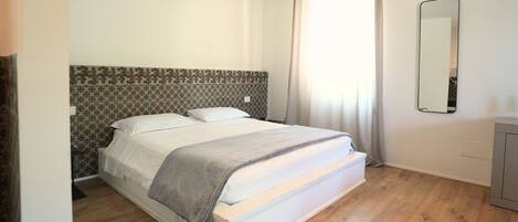 A bedroom with a bed, a headboard with a patterned design, a mirror, and a wooden floor.