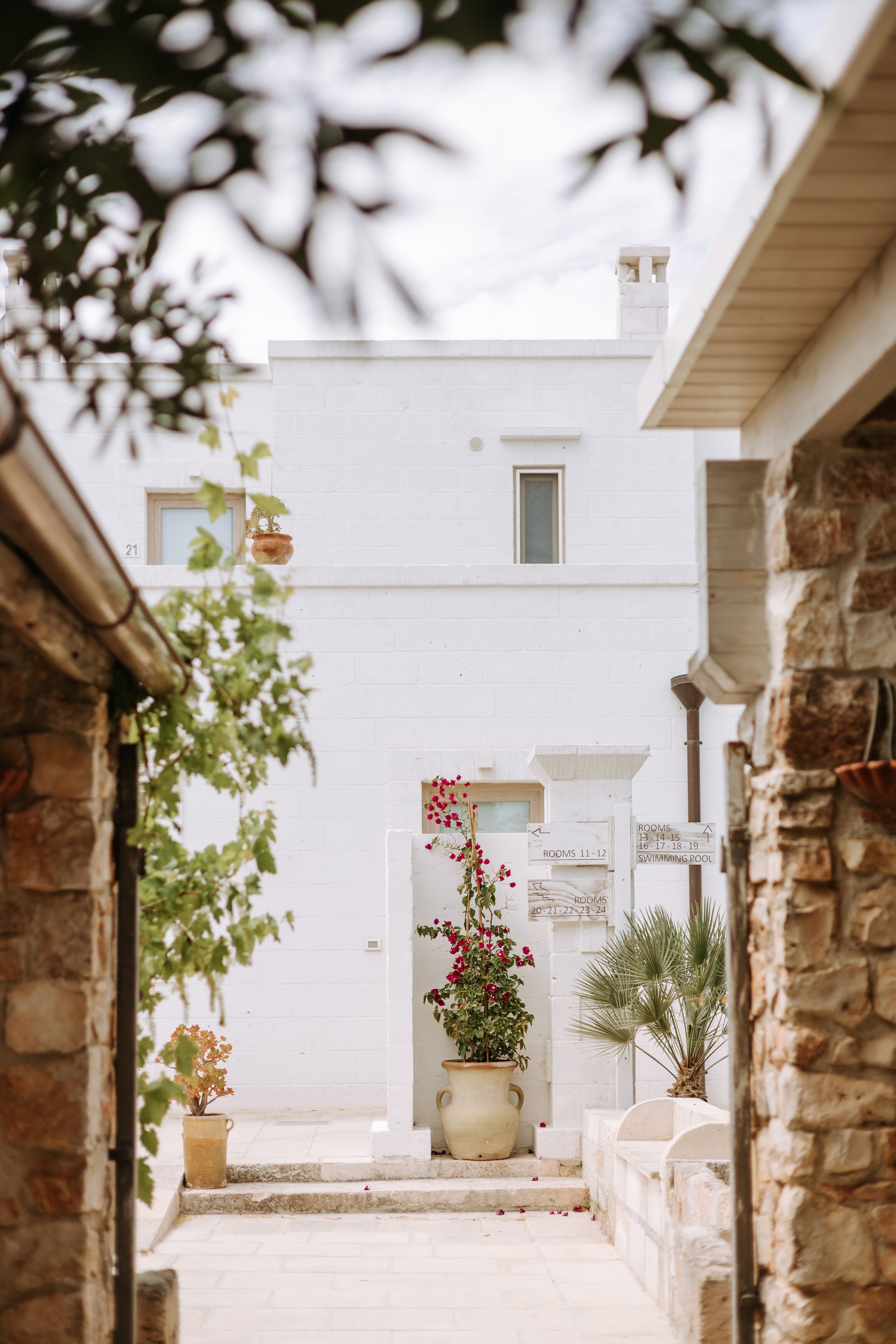 A narrow pathway leading to a white building with a small window and a door marked "ROOMS 11-12".