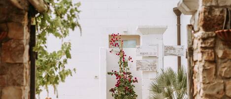 A narrow pathway leading to a white building with a small window and a door marked "ROOMS 11-12".