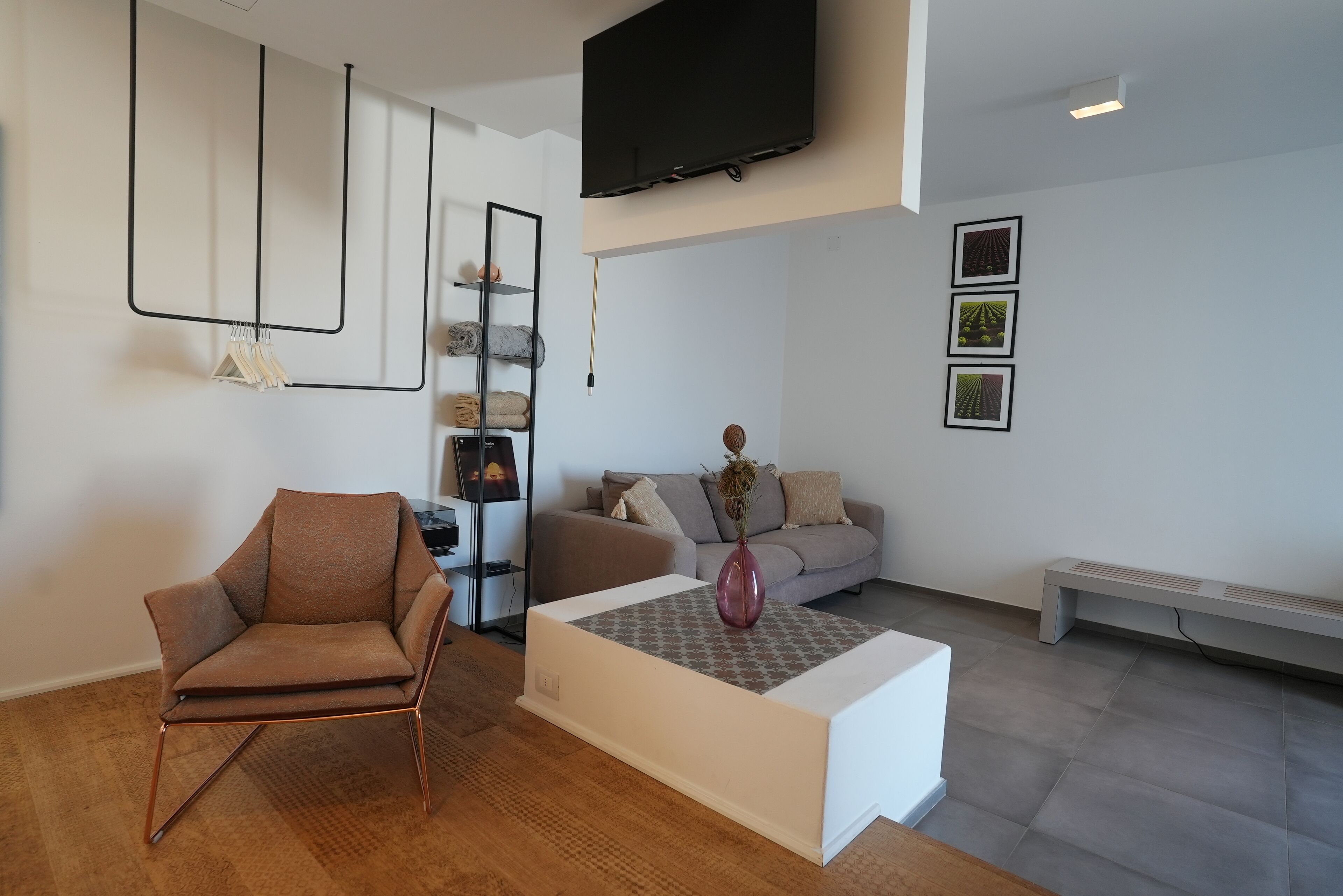 Uma sala de estar moderna com uma poltrona de couro marrom, uma mesa de centro branca, um sofá cinza e uma TV fixada na parede.