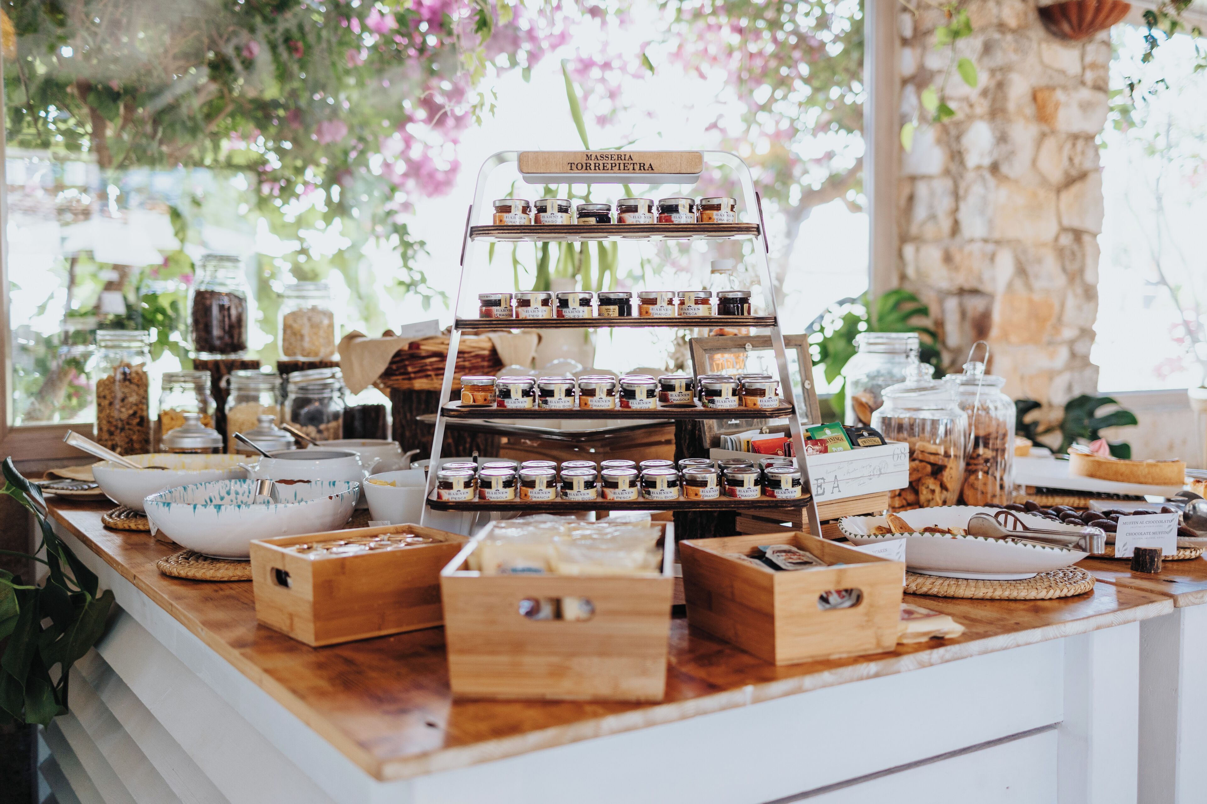 Une présentation de produits alimentaires avec des bocaux et des boîtes, une enseigne indiquant « MASSERIA TORREPIETRA », et un mur de pierre en arrière-plan.