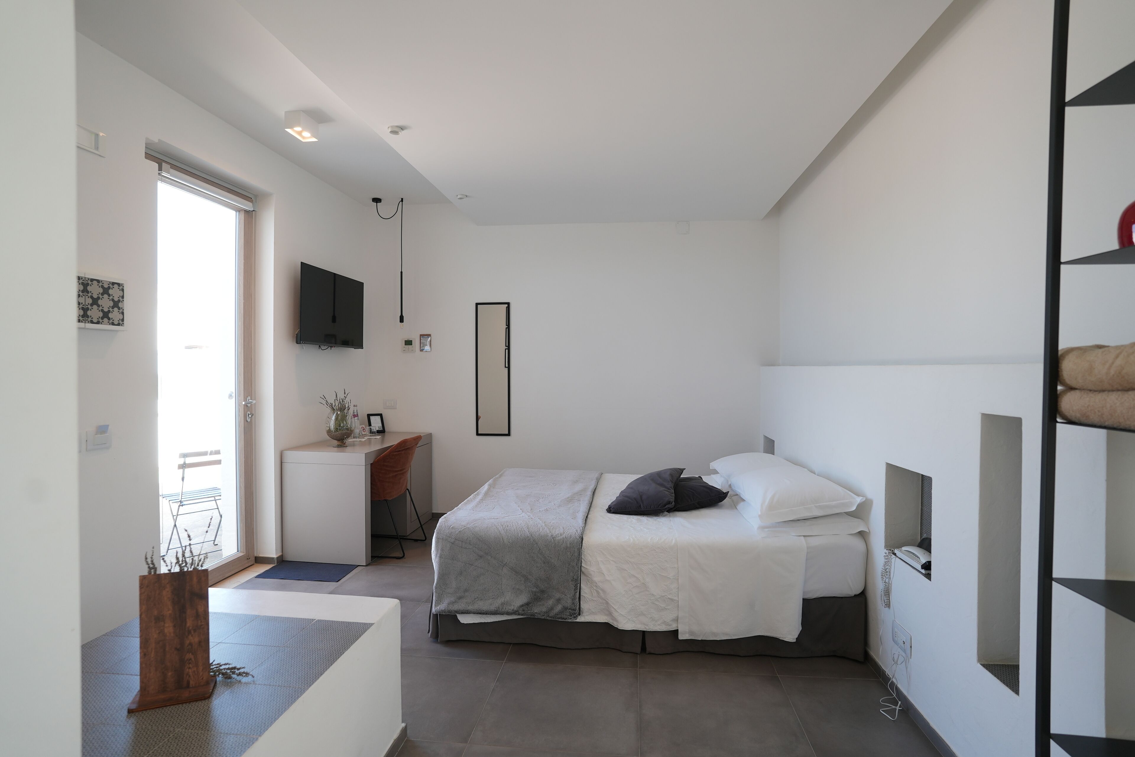 A modern bedroom with a bed, bedside table, and a TV mounted on the wall.