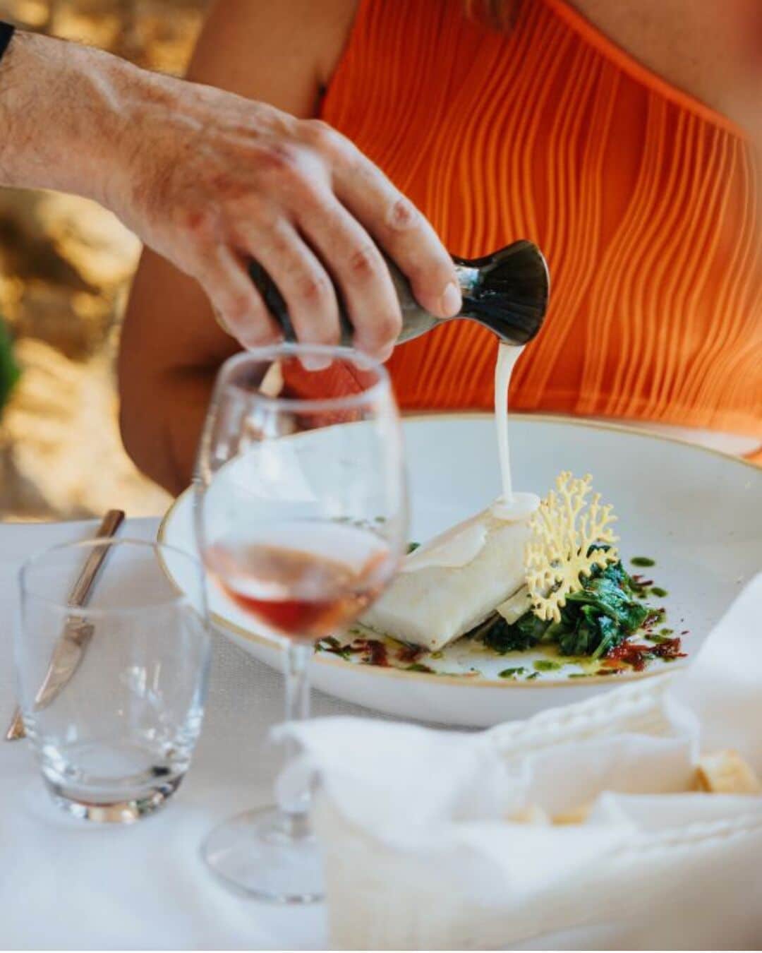 A person pouring a liquid from a bottle into a wine glass on a table.