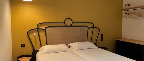 Uma cama com cabeceira, mesa de cabeceira e luminária pendente em um quarto com paredes amarelas.