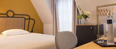 Habitación de hotel con cama, escritorio, silla, armario, espejo y ventana con cortinas.