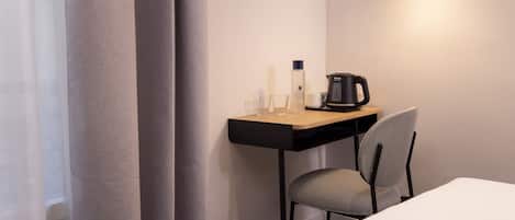 Una habitación de hotel con una cama, un escritorio con cafetera, una silla y una mesita.