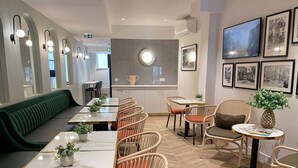 Interior de restaurante con un largo banco verde, varias mesas de comedor con sillas de mimbre y un televisor montado en la pared.
